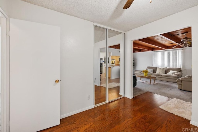 living area with a ceiling fan, wood finished floors, baseboards, beamed ceiling, and a textured ceiling