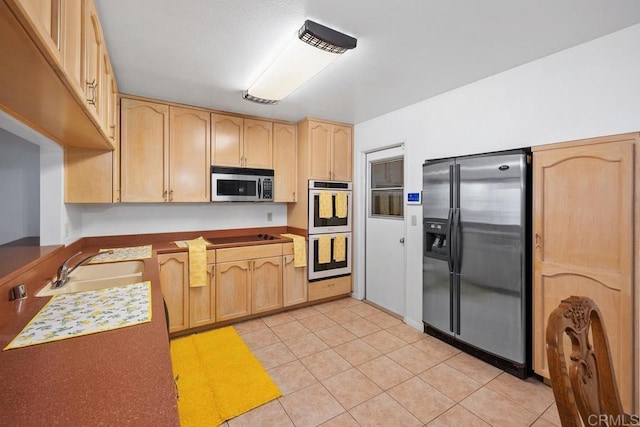 kitchen featuring stainless steel appliances, light brown cabinets, a sink, and light tile patterned flooring