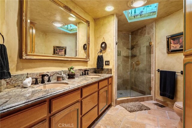 2743 Rodman Dr, Los Osos, CA 93402 - full bathroom featuring a skylight, a stall shower, stone tile floors, double vanity, and toilet