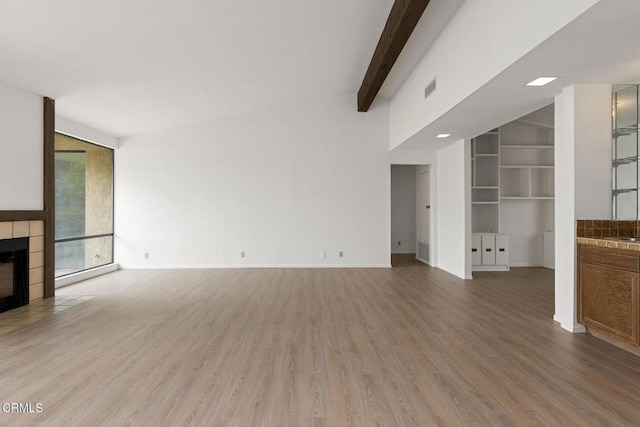 72460 Rodeo Way, Rancho Mirage, CA 92270 - unfurnished living room with light wood-style flooring, a tiled fireplace, beamed ceiling, and baseboards