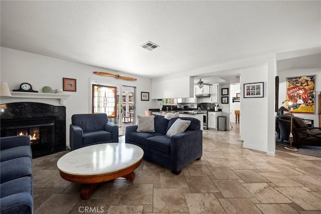 living area featuring stone tile flooring, ceiling fan, and a fireplace
