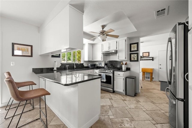 kitchen with stainless steel appliances, a peninsula, under cabinet range hood, a sink, and stone tile floors