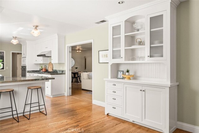 921 Arbutus Ave, Chico, CA 95926 - kitchen with under cabinet range hood, oven, white cabinets, white microwave, and a kitchen breakfast bar