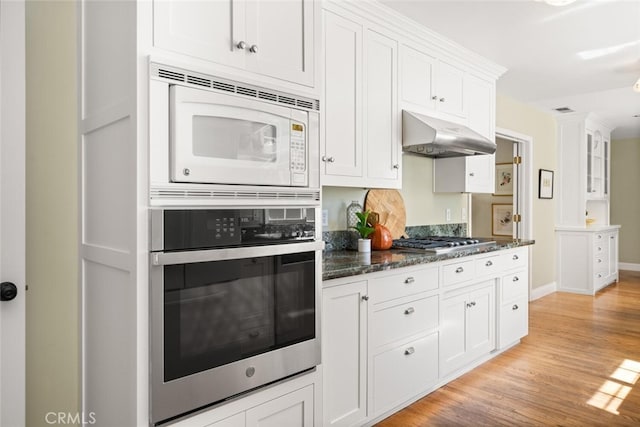 921 Arbutus Ave, Chico, CA 95926 - kitchen with appliances with stainless steel finishes, under cabinet range hood, white cabinets, light wood-style flooring, and dark stone countertops