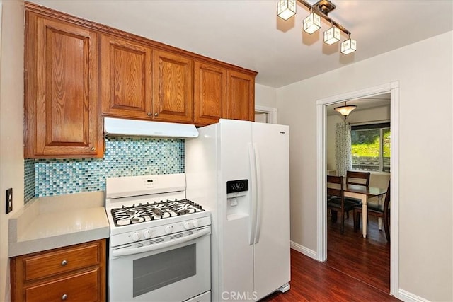 145 Cumberland Dr, Lake Arrowhead, CA 92352 - kitchen with white appliances, under cabinet range hood, brown cabinetry, decorative backsplash, and dark wood-style floors