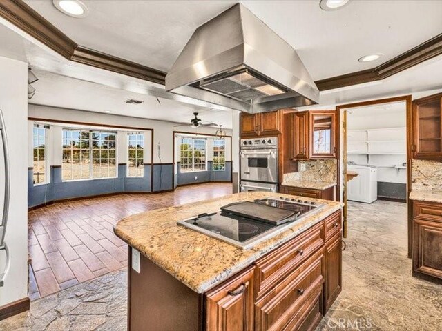 4689 Stirrup Ln Unit 29, Palms, CA 92277 - kitchen featuring island range hood, stovetop with downdraft, ornamental molding, washer / dryer, and decorative backsplash