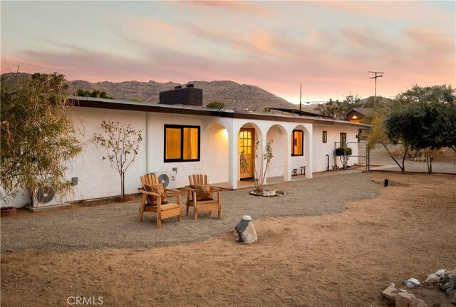 60515 Alta Loma Dr, Joshua Tree, CA 92252 - back of property at dusk with a chimney, stucco siding, a mountain view, and fence