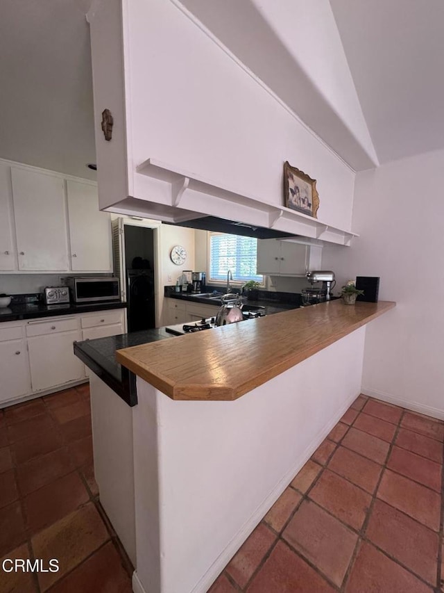 kitchen featuring stainless steel microwave, dark countertops, white cabinetry, a peninsula, and a kitchen breakfast bar
