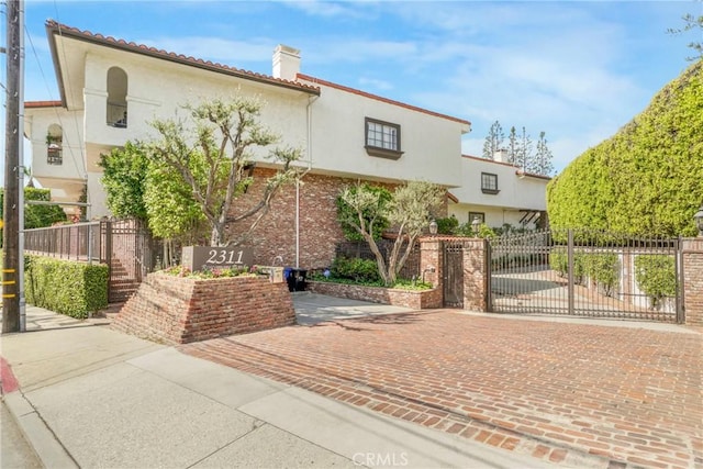 2311 Roscomare Rd Unit 16, Los Angeles, CA 90077 - mediterranean / spanish-style house featuring stucco siding, a chimney, and a gate