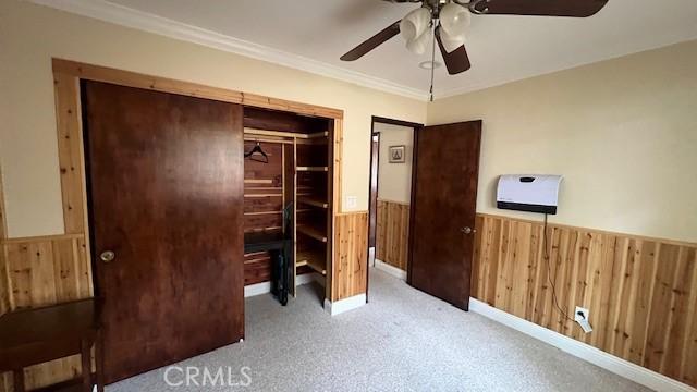 33421 Wild Rose Dr, Green Valley Lake, CA 92341 - unfurnished bedroom featuring a wainscoted wall, wood walls, carpet floors, crown molding, and ceiling fan