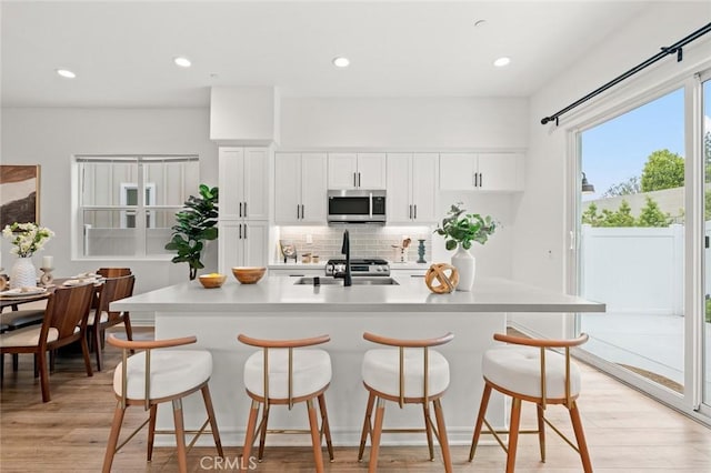 937 E Wonder Ln, Glendora, CA 91740 - kitchen featuring stainless steel microwave, a breakfast bar area, backsplash, white cabinets, and light wood-style floors