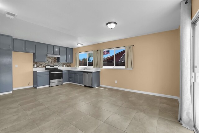 1018 N Millard Ave, Rialto, CA 92376 - kitchen featuring appliances with stainless steel finishes, light countertops, under cabinet range hood, gray cabinetry, and backsplash