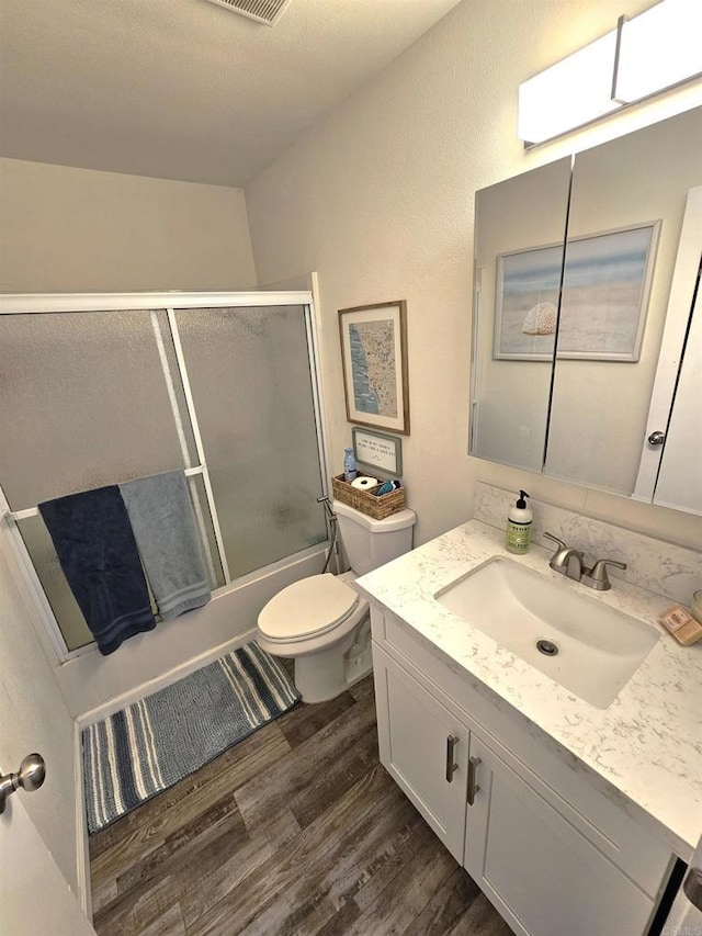 bathroom featuring wood finished floors, toilet, bath / shower combo with glass door, and vanity