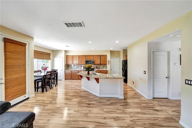 kitchen with stainless steel microwave, light wood finished floors, freestanding refrigerator, decorative backsplash, and baseboards