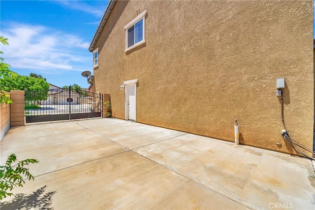 view of side of home featuring stucco siding, fence, a patio, and a gate