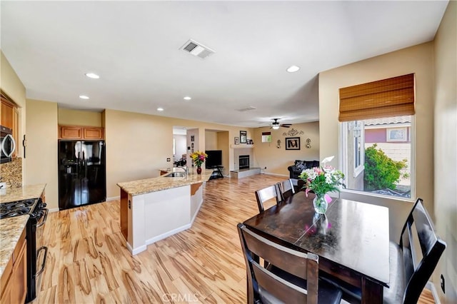 dining room with light wood-style flooring, ceiling fan, recessed lighting, baseboards, and a glass covered fireplace