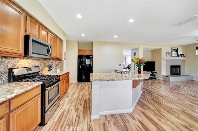 kitchen featuring stainless steel appliances, light wood finished floors, tasteful backsplash, a sink, and light stone counters