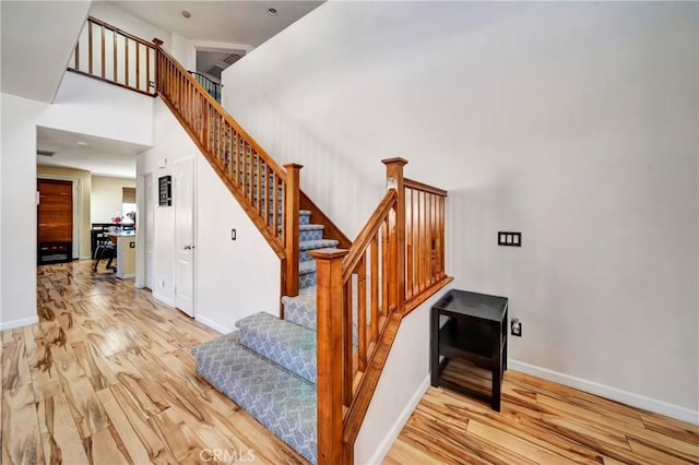 stairway with wood finished floors, baseboards, and a towering ceiling