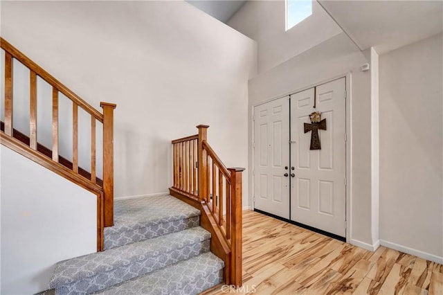 entrance foyer with stairs, a high ceiling, wood finished floors, a skylight, and baseboards