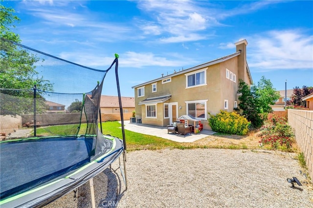 rear view of house featuring a trampoline, stucco siding, a fenced backyard, and a patio