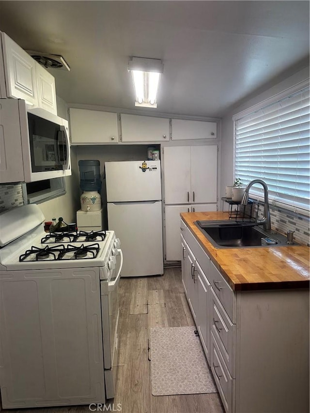 kitchen featuring white appliances, butcher block counters, a sink, light wood-type flooring, and white cabinetry