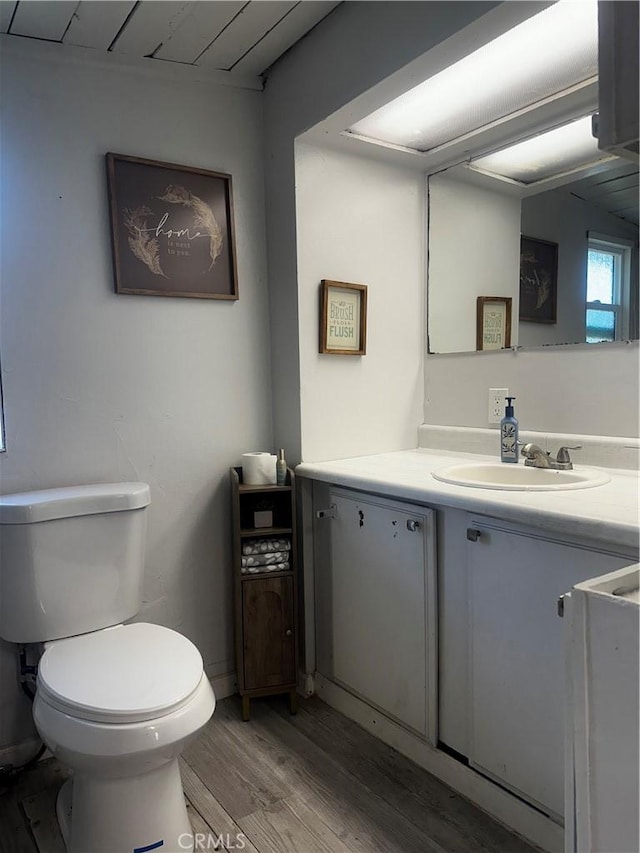 half bath featuring wood finished floors, vanity, and toilet