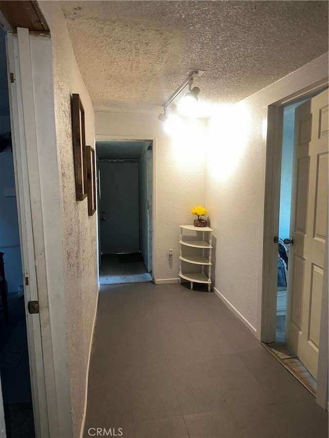 hall with a textured ceiling and a textured wall