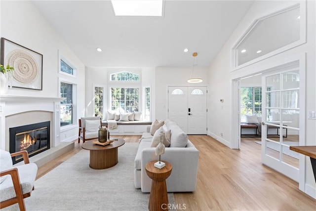 living room with healthy amount of natural light, light wood finished floors, a glass covered fireplace, recessed lighting, and high vaulted ceiling