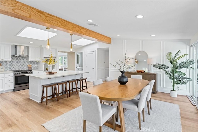 dining room with a skylight, light wood-type flooring, beamed ceiling, and recessed lighting