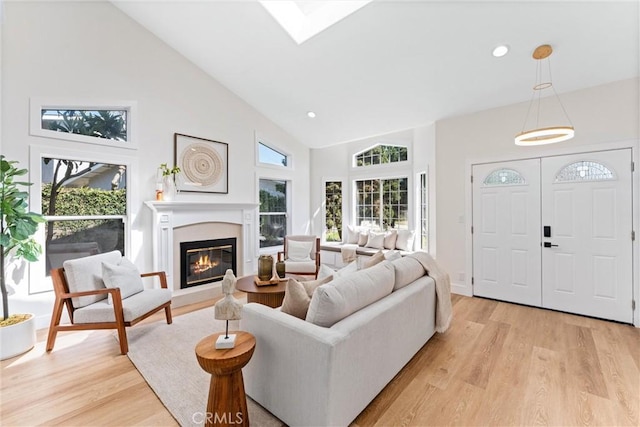 living area with high vaulted ceiling, light wood-style flooring, a glass covered fireplace, and recessed lighting