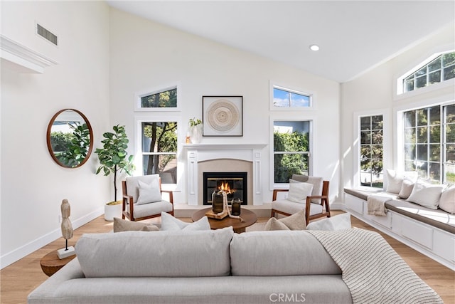 living room featuring high vaulted ceiling, a glass covered fireplace, baseboards, light wood-type flooring, and recessed lighting