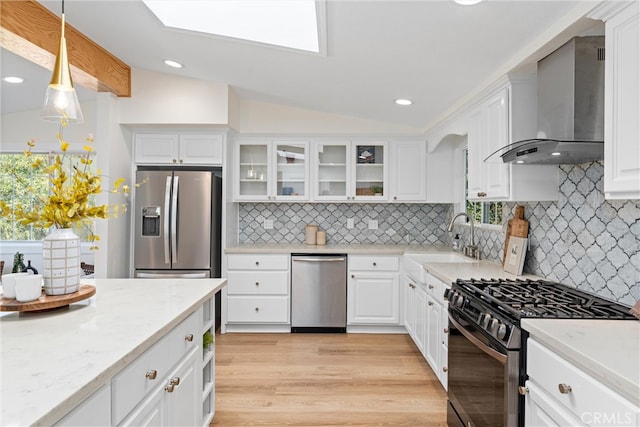 kitchen with wall chimney exhaust hood, appliances with stainless steel finishes, a sink, lofted ceiling, and white cabinets