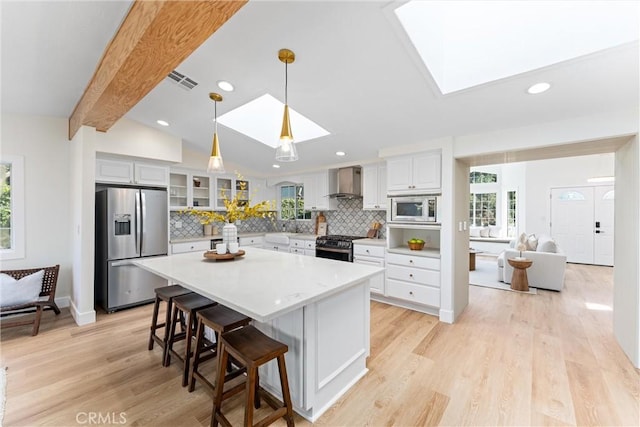 kitchen with stainless steel appliances, wall chimney exhaust hood, a skylight, healthy amount of natural light, and recessed lighting