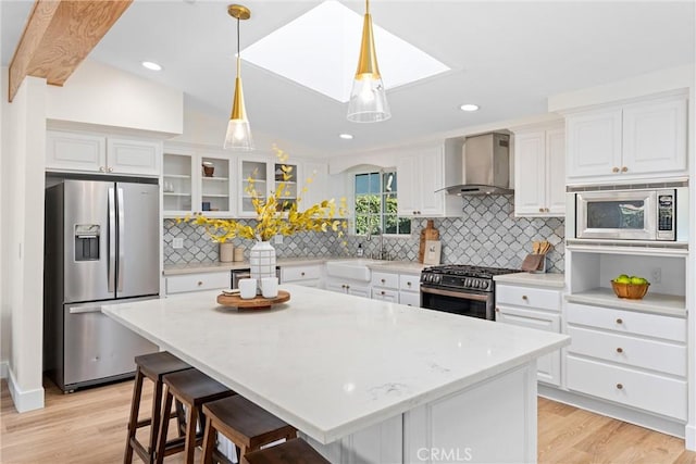 kitchen with appliances with stainless steel finishes, wall chimney exhaust hood, a sink, light wood-style flooring, and recessed lighting