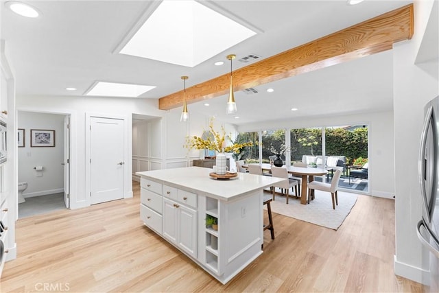 kitchen with a skylight, recessed lighting, beamed ceiling, white cabinets, and light wood-type flooring
