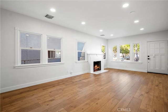 unfurnished living room featuring a warm lit fireplace, light wood-style flooring, baseboards, and recessed lighting