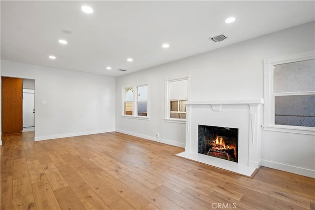 unfurnished living room with a warm lit fireplace, light wood-style floors, baseboards, and recessed lighting