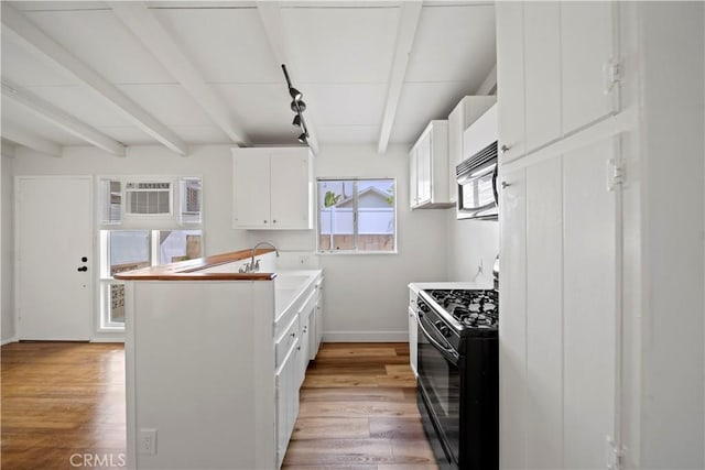 kitchen featuring black range with gas stovetop, a sink, baseboards, white cabinets, and beam ceiling