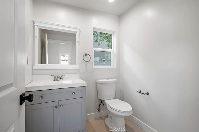 half bath with baseboards, toilet, and vanity