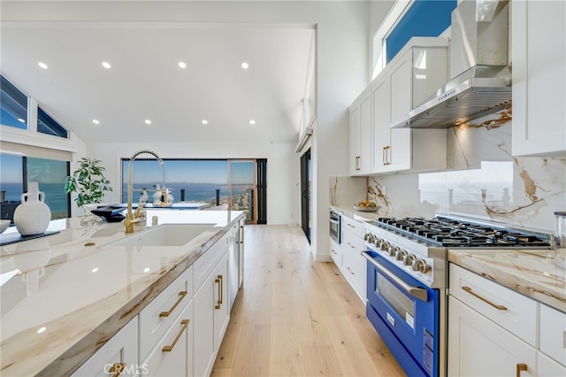 7655 Caminito Avola Ln, Jolla, CA 92037 - kitchen featuring high end stove, wall chimney range hood, light wood-type flooring, white cabinetry, and a sink