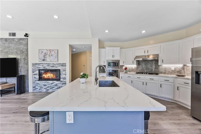18680 Vantage Pointe Dr, Rowland Heights, CA 91748 - kitchen featuring stainless steel appliances, under cabinet range hood, a glass covered fireplace, white cabinets, and light stone counters