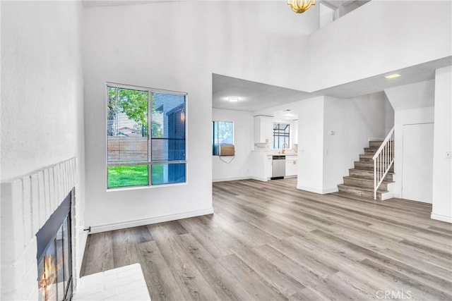 15696 Paine St, Fontana, CA 92336 - unfurnished living room featuring stairs, a towering ceiling, a brick fireplace, light wood-type flooring, and baseboards