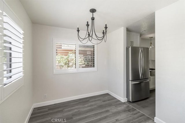 unfurnished dining area with a chandelier, dark wood-style flooring, and baseboards