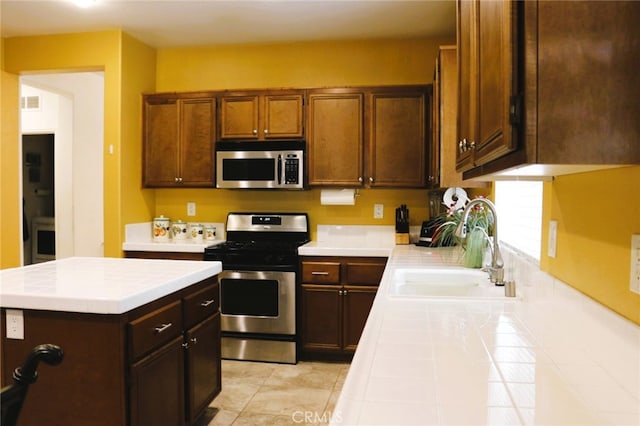13217 Acacia Ave, Moreno Valley, CA 92553 - kitchen with stainless steel appliances, a sink, tile counters, a center island, and light tile patterned floors