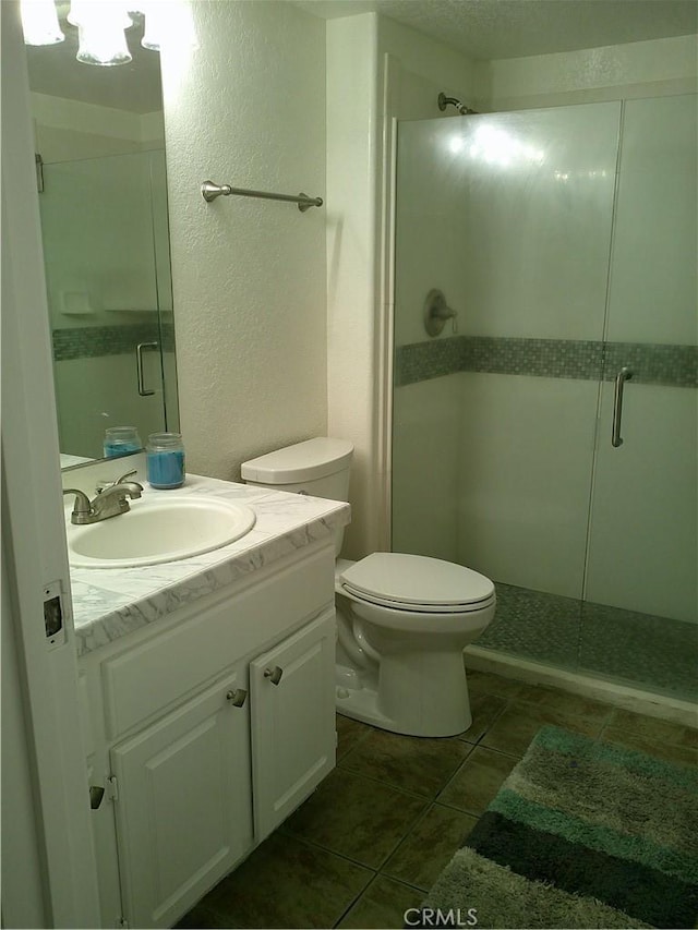full bath with a stall shower, toilet, tile patterned floors, a textured wall, and vanity