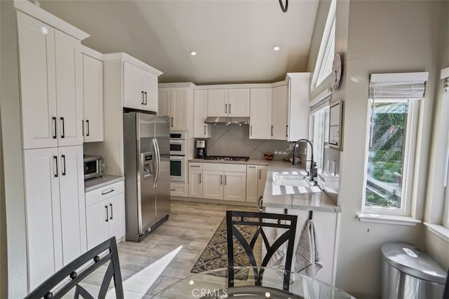 kitchen featuring a sink, stainless steel appliances, light countertops, under cabinet range hood, and lofted ceiling