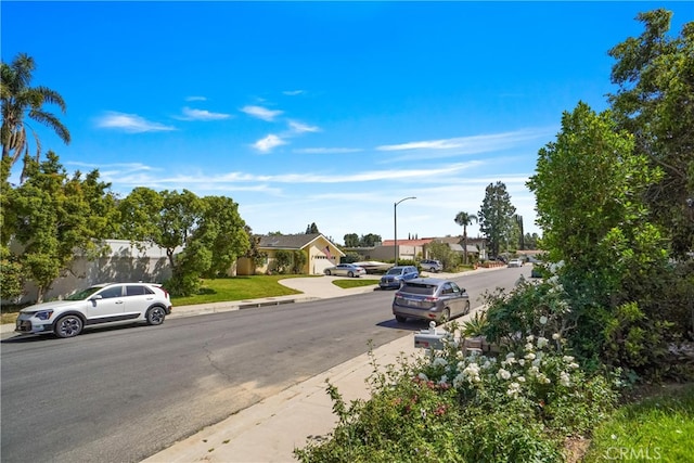 view of asphalt road with street lights, a residential view, curbs, and sidewalks