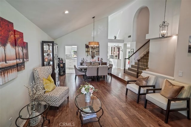 living room featuring a chandelier, high vaulted ceiling, dark wood-type flooring, stairs, and arched walkways