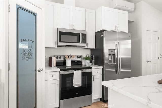 6333 Graham Rd, Paradise, CA 95969 - kitchen with stainless steel appliances, a wall mounted AC, white cabinets, light stone counters, and light wood-style floors