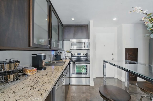 140 Linden Ave Unit 615, Long Beach, CA 90802 - kitchen with appliances with stainless steel finishes, dark brown cabinetry, concrete flooring, light stone counters, and a sink